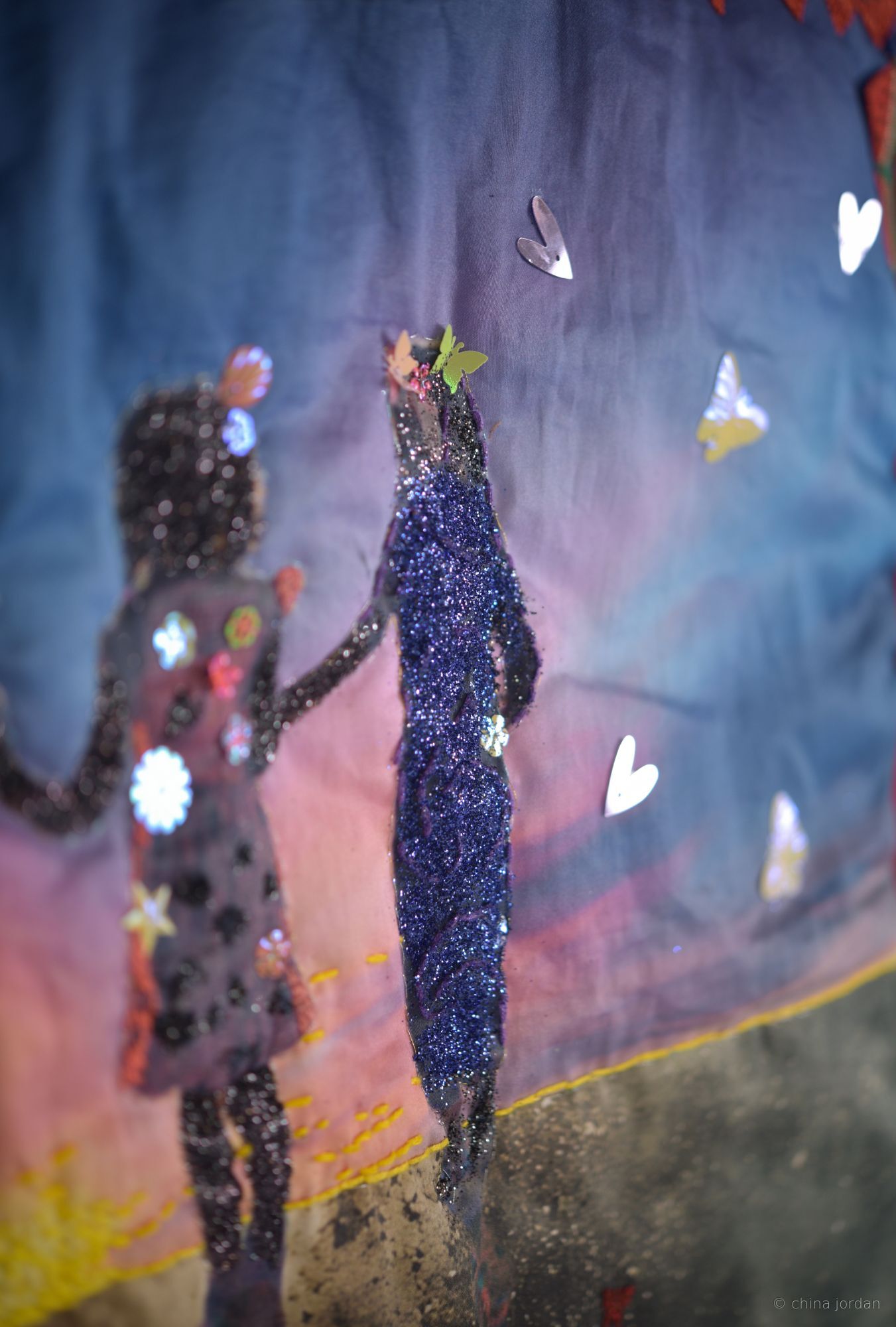 Care (close-up detail) — glitter-embellished silhouettes against sunset sky