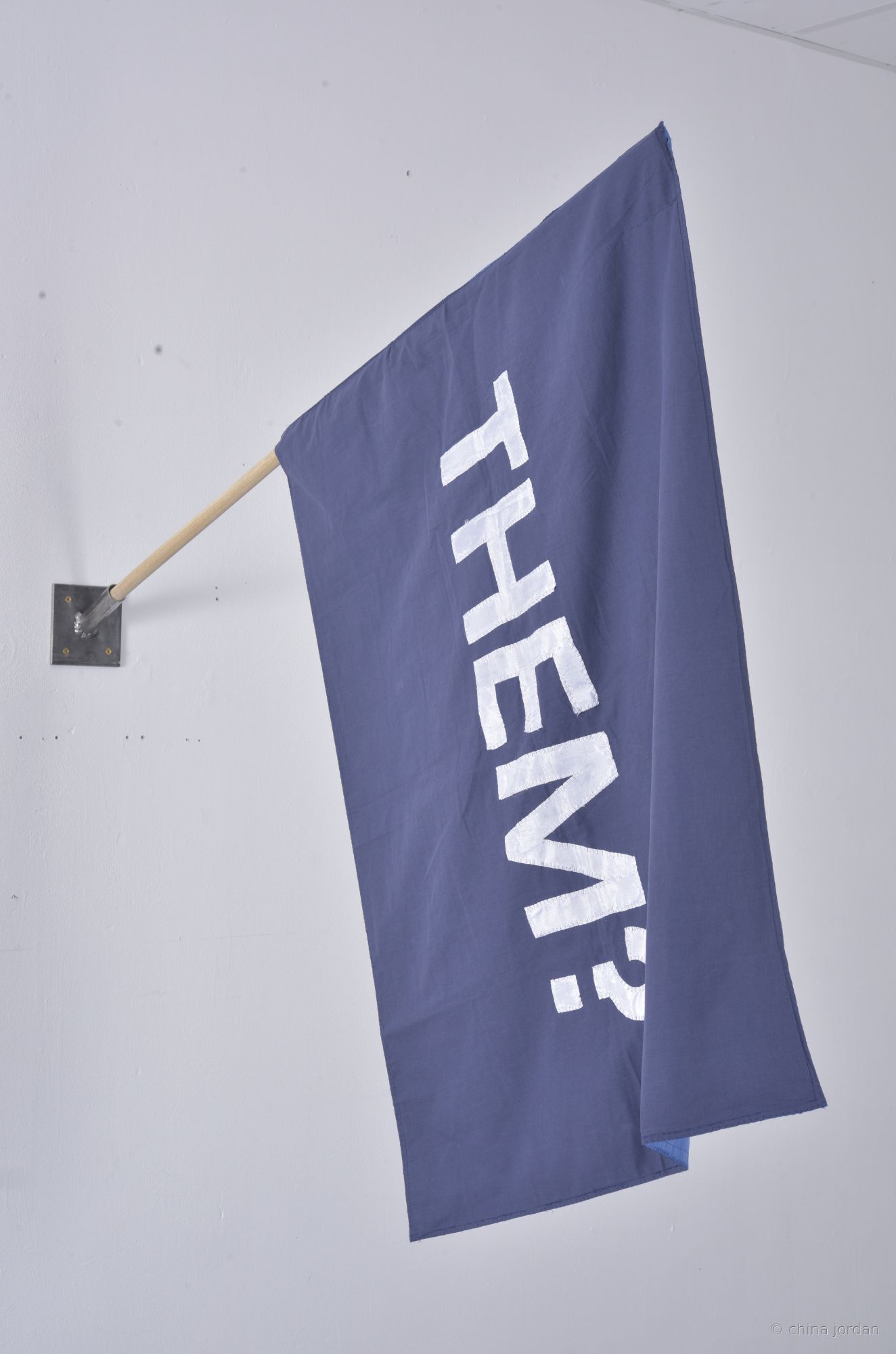 THEM? — appliqu&eacute;d blue-grey fabric flag on wooden pole